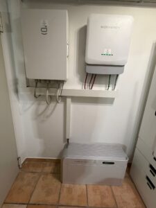 Installation eines Sigenergy SigenStor Systems bestehend aus einem weißen Sigen Inverter (Wechselrichter) an der Wand und einem flachen Sigen Battery-Modul am Boden in einem Technikraum.