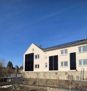 Mehrfamilienhaus mit schwarzen Full-Black Solarmodulen an der hellen Fassade und einer klassischen Photovoltaik-Anlage auf dem Satteldach zur optimalen Energiegewinnung im Winter.