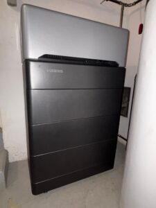 Ein WEESS Solarspeicher-Turm bestehend aus vier dunklen Batteriemodulen und einer silbernen Steuereinheit (BMS) an der Spitze, installiert in einem Technikraum zur Speicherung von Photovoltaik-Energie.